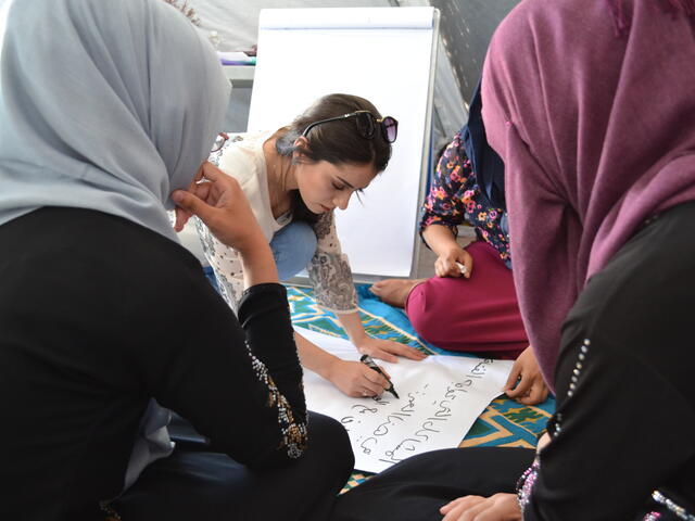 The IRC's Zaytoon Saeed writes on a poster as she leads teenage girls in a negotiation skills activity at the IRC's women's center.