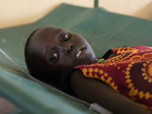 A young girl undergoing treatment for cholera lies on a cot, hooked up to an intravenous drip.