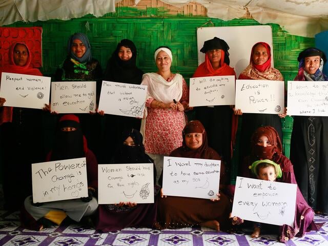 Razia Sultana stands with women holding signs with empowering messages about women that have been part sessions in her centre 