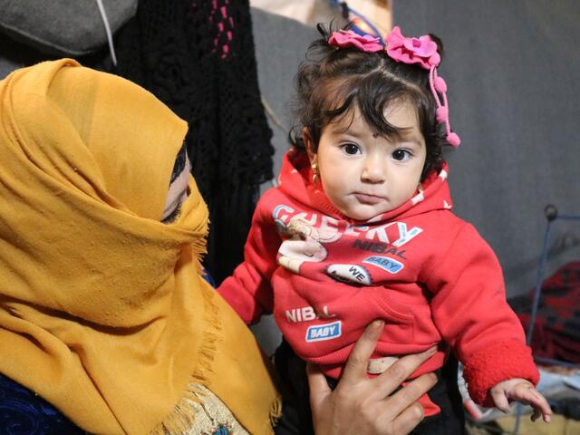 Um Tamer cradles her daughter Zainab in her tent in Areesha refugee camp in Syria. 