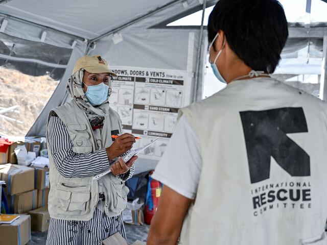 Rahima standing in a tent with a clipboard and talking to an IRC staff member