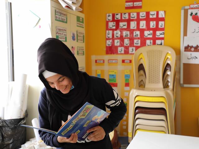 Girl in a classroom smiles whilst reading a book.