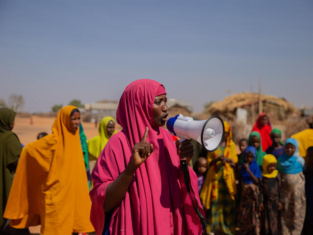 Woman speaks down a megaphone to a crowd of women and children in Helowyn camp in Ethiopia.