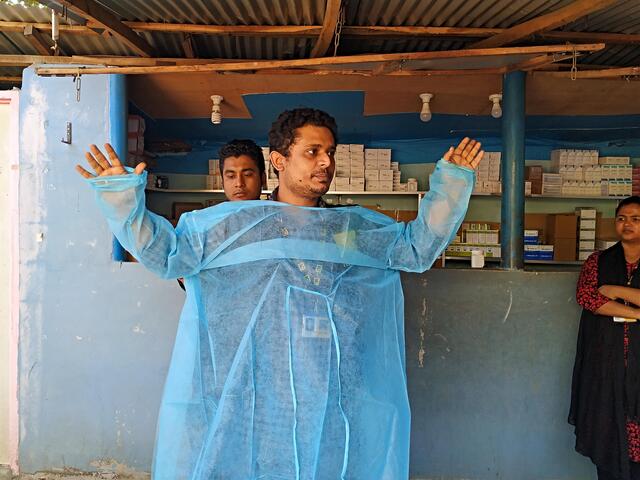 Dr Hossein demonstrates how to wear PPE, putting on a blue medical gown.