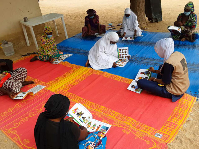 Aishatu sitting with clients on a rug.