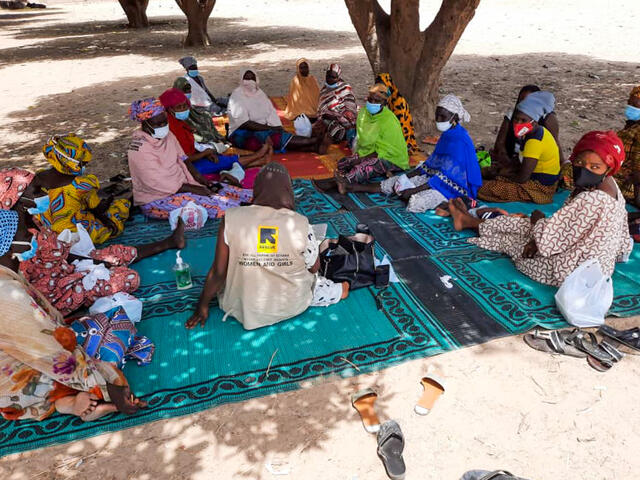 An IRC staff member talking with a group of women all seated on the floor