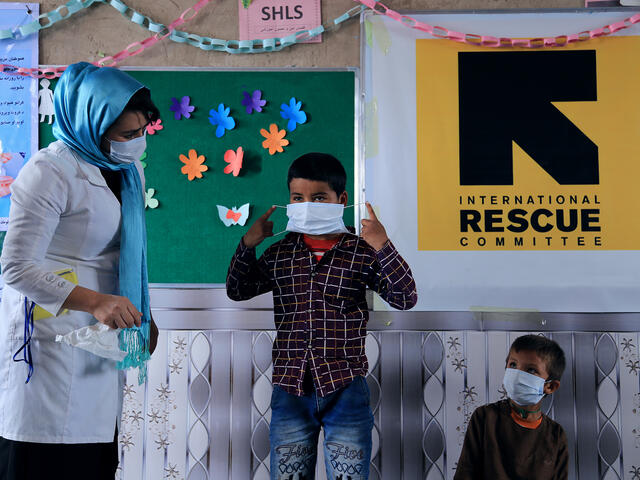IRC female health staff teaches children in the classroom the correct way to wear a mask.