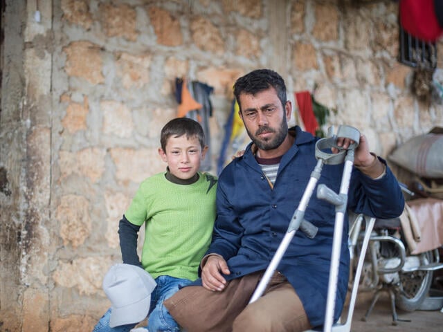 10 year old Faisal sits with his father outside hims home in Syria.