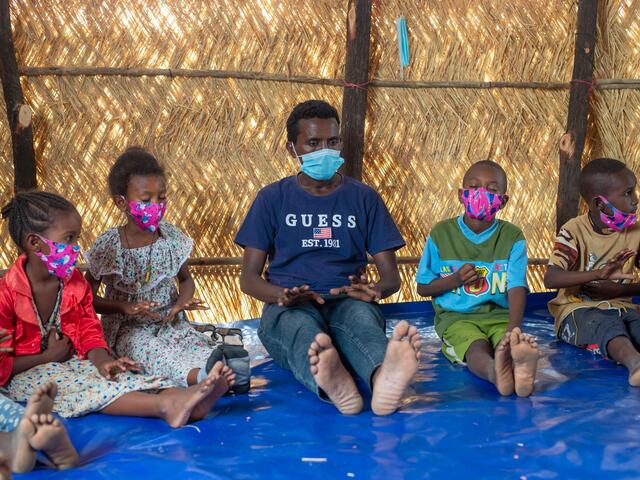 A man, Hadera, and children sitting on the floor partaking in mindfulness breathing activities at an IRC safe and healing space in Sudan