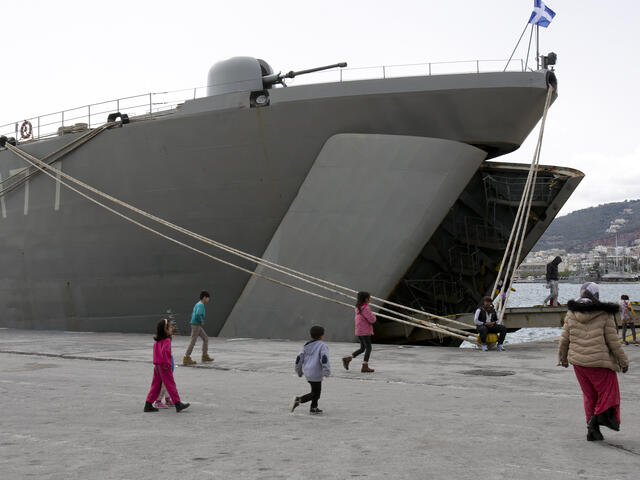 Refugees walk on a dock next to a Greek Navy ship on the Island of Lesbos