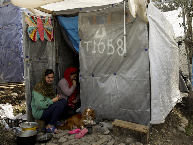 Parasi, a woman who came to Lesvos from Afghanistan, and a friend, sit outside their shelter with their dog Rex. 
