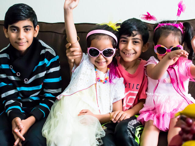 Syrian children resettled in San Diego pose for a silly photo on their couch while playing dress-up.