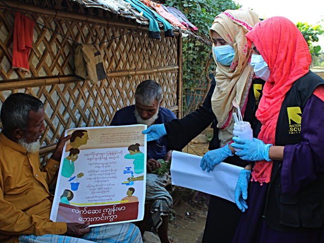 Two women who are IRC community health volunteers wear masks as they distribute information about the coronavirus to two men in the Cox's Bazar refugee camp