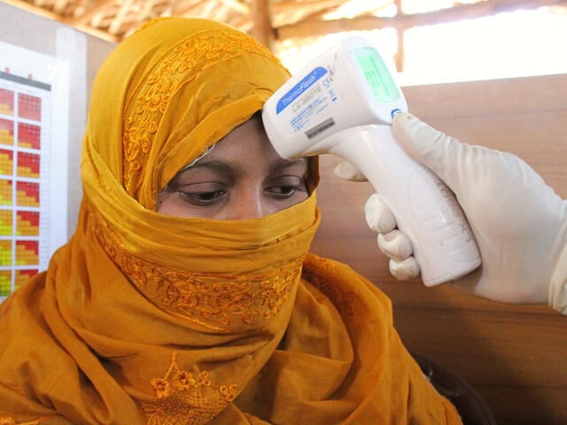 Sakera Akter, 22, sits with a thermal scanner thermometer pointed at her head to check for fever