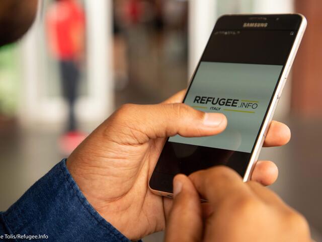 CLose-up of a person holding a cellphone with a Refugee.Info page on screen