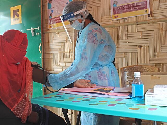 An IRC midwife wearing a mask, face shield and protective suit takes the blood pressure of a patient with a veil covering her face as a precaution during the coronavirus pandemic.