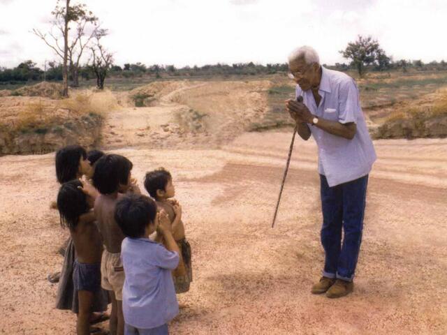 Bayard Rustin bends and clasps his hands in greeting while meeting a group of refugee children.