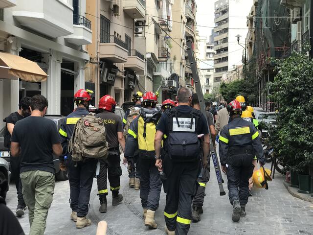 A group of Beirut firefighters responding to the explosion walk down a street 