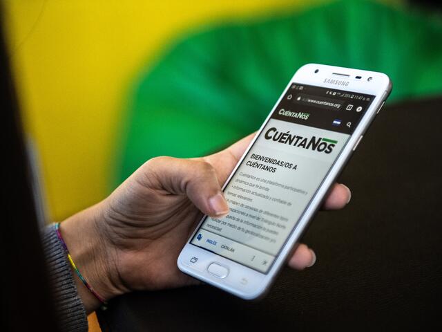 Close-up of a smartphone displaying the Cuentanos.org website in a women's hand
