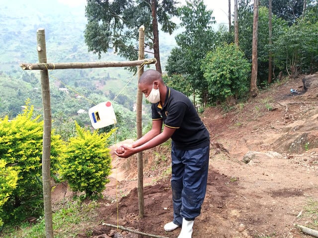 An IRC staff member in Uganda demonstrates the use of a handwashing station fashioned from sticks, rope, and a large plastic water jug.
