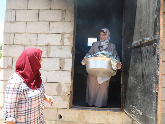 Syrian nurse and IRC community volunteer Mariam carries medical supplies out of a building while speaking with another woman outside the door