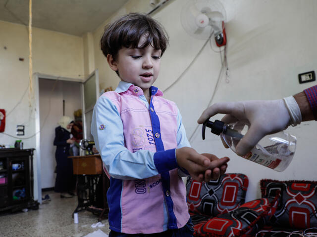 Five-year-old Murad holds his hands out as his father puts hand sanitizer on them inside their home in Syria during the COVID-19 pandemic.