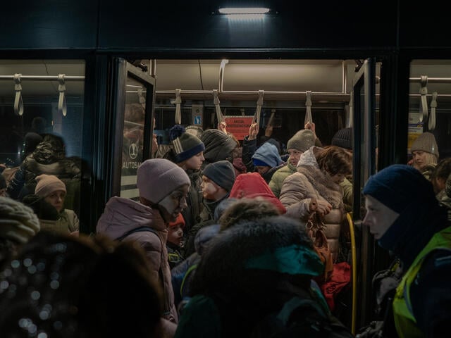 Refugees from Ukraine in winter coats wait to board a bus at the Ukraine-Poland border.
