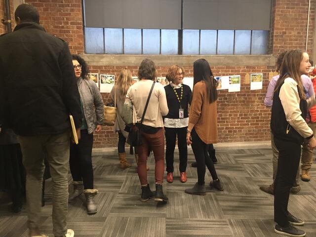 New Roots program members gather to look at photography along the brick wall.