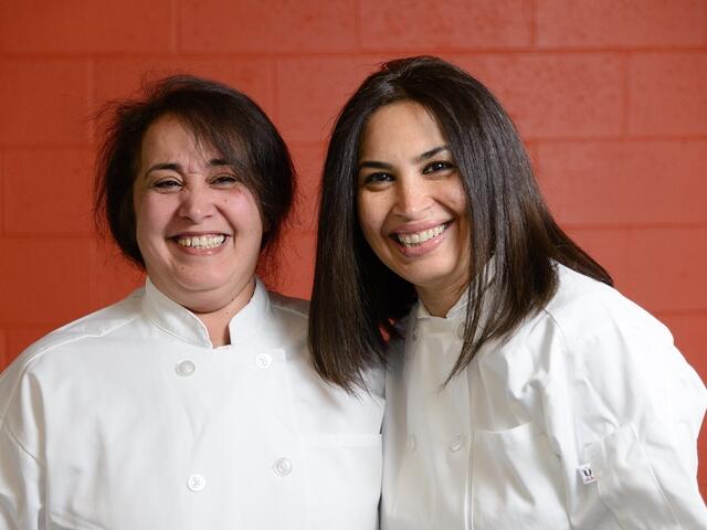 Suha and  Mayyadah pose in chef's coats for a picture.