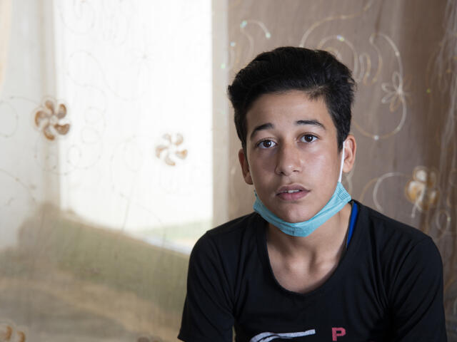 Fifteen-year-old Muhammad, wearing a mask around his chin, sits and looks at the camera. 