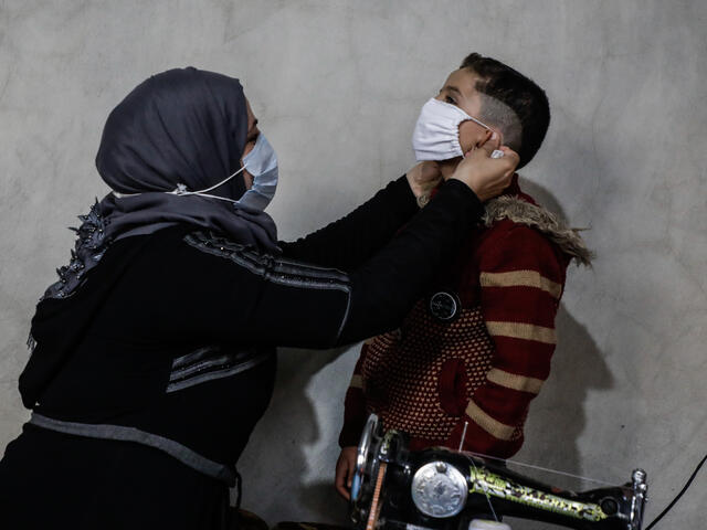 Um Abdo puts a face mask she has sewn on her young son, inside their tent in Idlib, Syria.