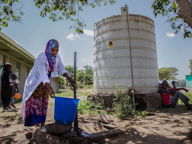 An IRC health worker in Ethiopia collects water in a large bucket.
