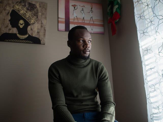 Fredrick Shema sitting on a stool in his home next to a window. 