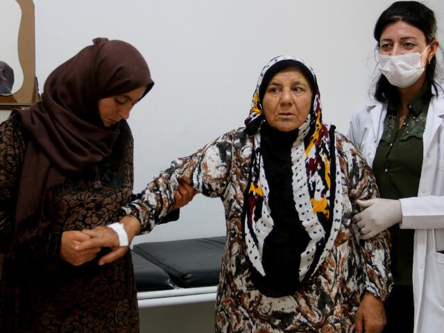 An elderly patient holds onto her daughter and the doctor as she leaves her consultation at a clinic run by the local health authorities with support from the IRC in Amuda, northeast Syria.