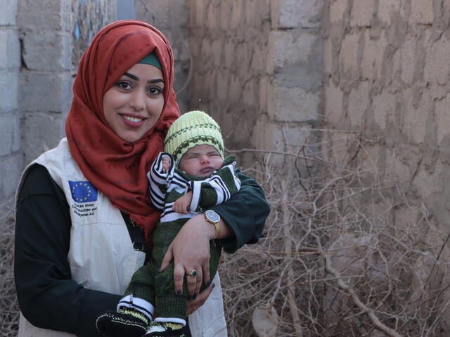 A smiling Dr. Bushra Al-Aghbari holds a sleeping infant boy in Yemen.
