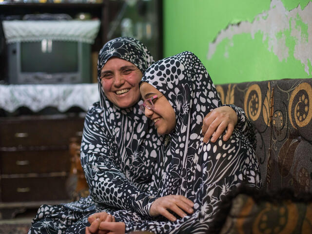 Salam and her mother, wearing matching outfits, sit in a couch and laugh together. 