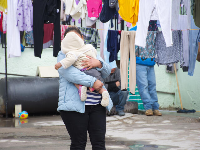 Alma, an asylum seeker from Guatemala, with her toddler daughter at an IRC-supported shelter in Mexico. She is holding her daughter while laundry dries near them.