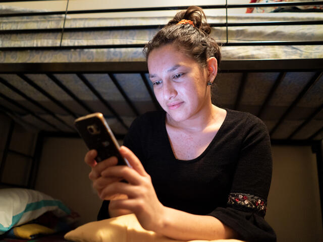 Valentina, 23, from El Salvador, sits on her bed talking to her sister on her cell phone. 