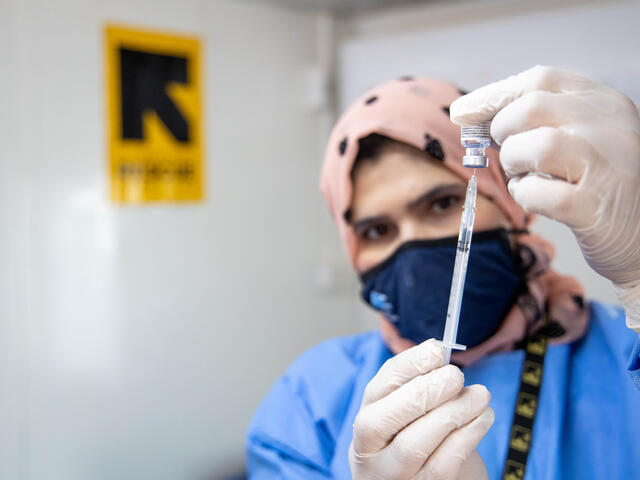 A nurse wearing PPE draws COVID-19 vaccine into a syringe inside an IRC health climic in Zaatari refugee camp, Jordan