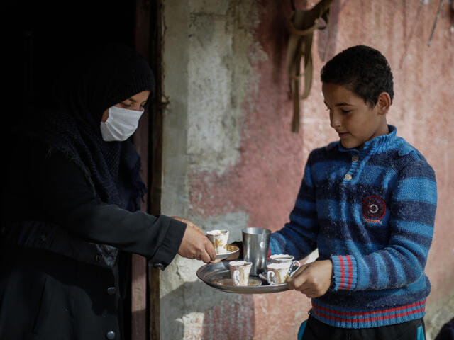Tareq holds a tray with a tea pot and tea cups and offers it to his mom 