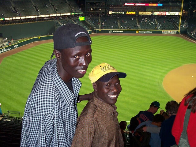 Two young Sudanese men, from the group of refugees known as the "Lost Boys" of Sudan, smile in a photo taken from their seats at a baseball game in the U.S.