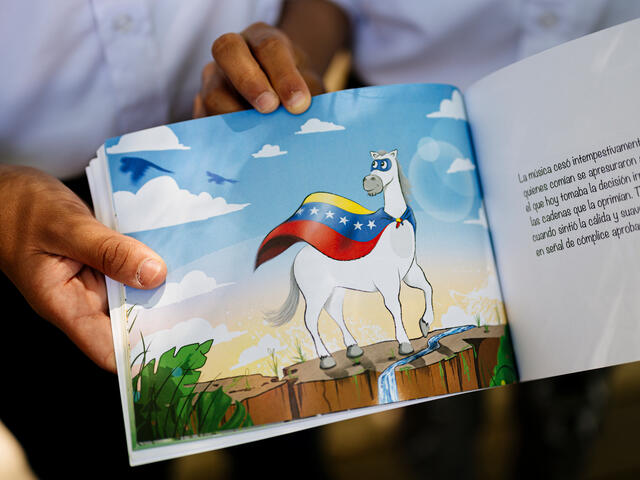 Leander's and Jesus's book opened to a page showing a white animal waring a tricolor flag around its neck on the left page, and text in Spanish on the right page.