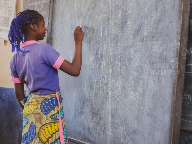 Kauvaumah, 11, smiles as she stands writing at a blackboard in her classroom in northern Cameroon.