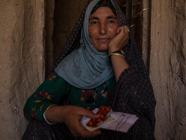 A  35-year-old Afghan widow sits in a doorway holding packets of medication she was able to get with the IRC's support.