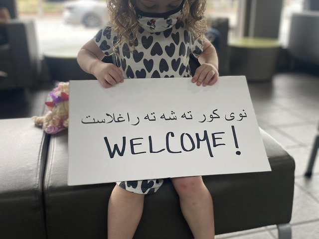 A young girl holds a "Welcome" sign in Pashto and English.