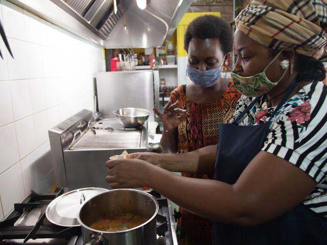 Two women wearing masked cook together over a stove.