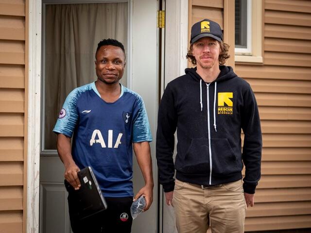 IRC employment specialist Nick Smith stands with his client, a refugee man who is holding a laptop from the IRC to assist him with his job search.