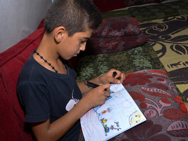 A Syrian boy draws clouds on a piece of paper.