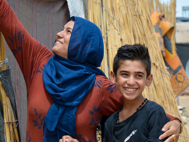 A Syrian mother and her son hug and smile outside a tent.