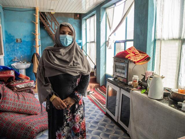 Noor stands in a sunny kitchen with blue walls.